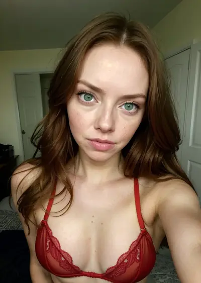 A woman with long brown hair and green eyes is wearing a red lace bra. She is looking directly at the camera with a neutral expression. Her face, neck, and upper chest are visible…